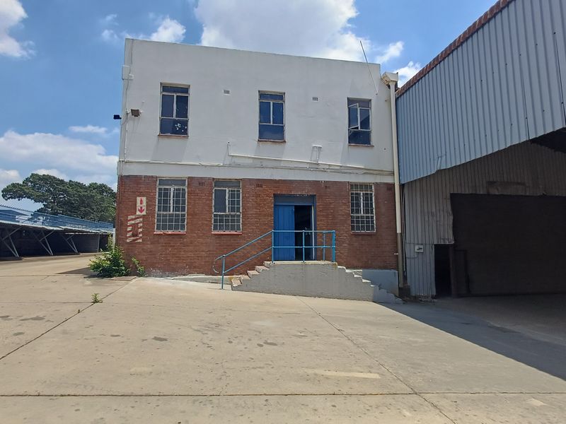 Industrial property exterior featuring a two-story brick and plaster building with adjacent warehouse structure, concrete yard, and metal security railings.