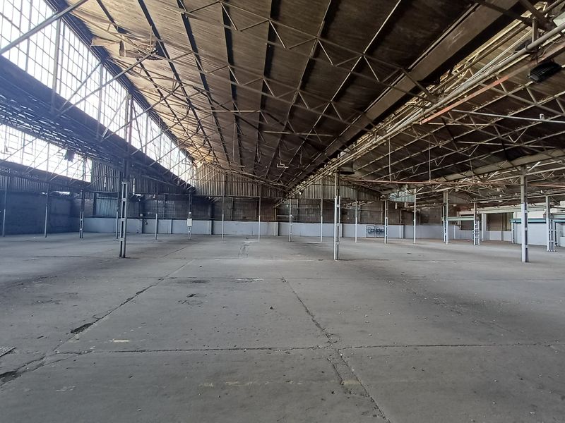 Expansive industrial warehouse space featuring high ceilings, exposed steel truss roof structure, large clerestory windows, and durable concrete flooring.