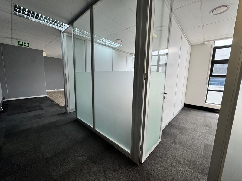 Modern office space featuring glass partition walls, frosted privacy panels, suspended ceilings with recessed lighting, and durable carpet tiles in a professional layout.