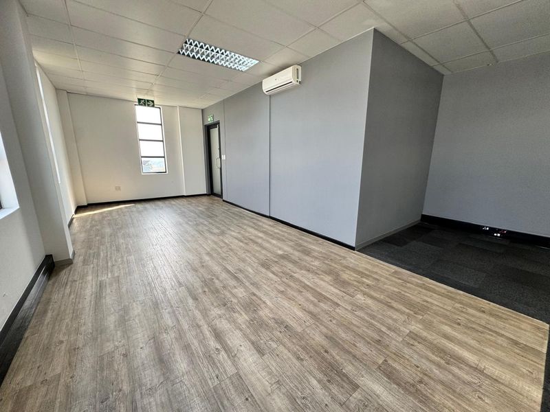 A clean, vacant office space featuring a mix of laminate and carpet flooring, suspended ceilings, and a wall-mounted air conditioning unit.