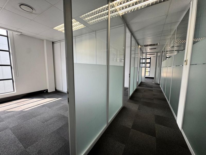 Modern office space featuring glass partition walls, carpeted flooring, and a suspended ceiling with recessed lighting, providing a clean and professional work environment.