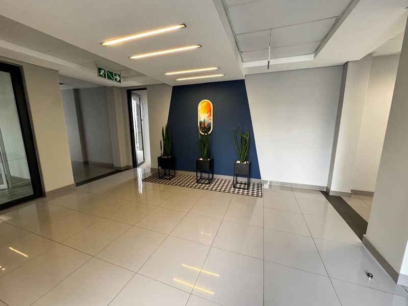 A bright and modern office entrance lobby featuring polished tiled flooring, recessed linear lighting, and a clean, professional aesthetic.