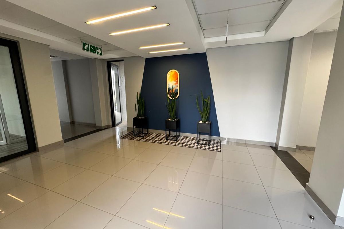 A bright and modern office entrance lobby featuring polished tiled flooring, recessed linear lighting, and a clean, professional aesthetic.