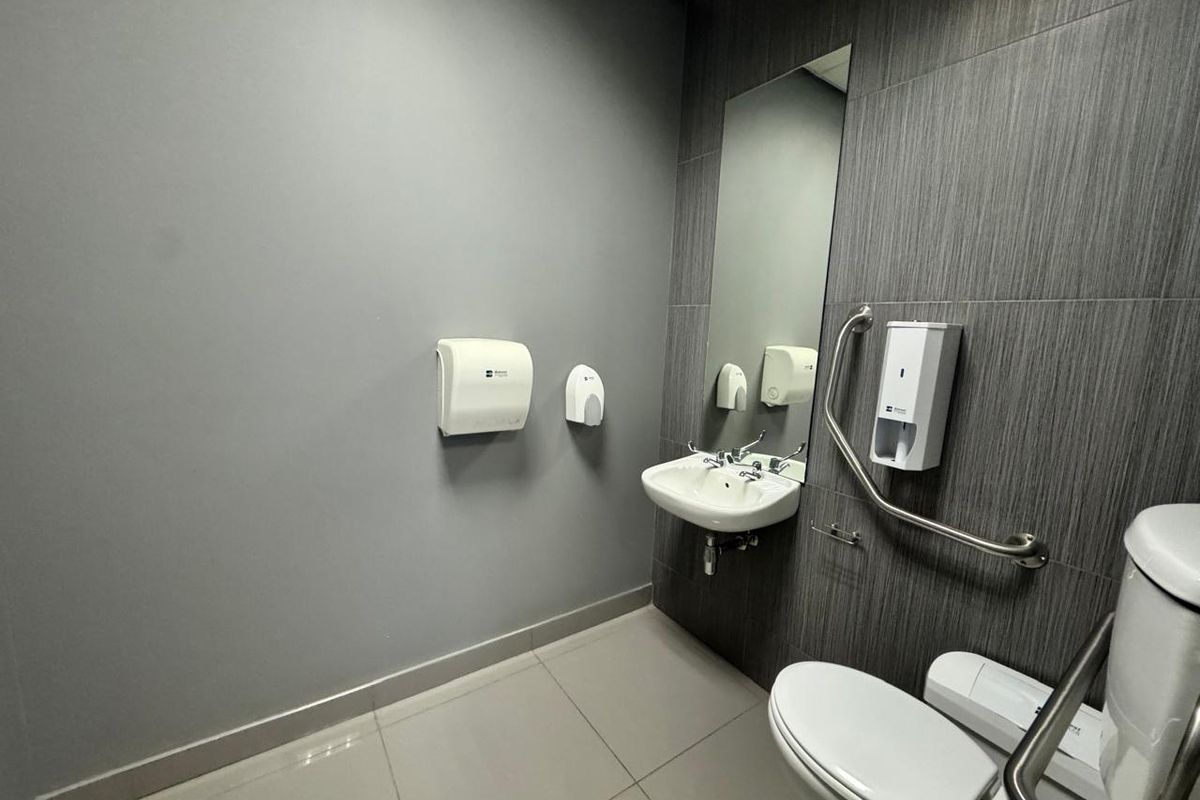 A clean, modern accessible bathroom featuring tiled walls, a wall-mounted sink, toilet, and safety grab rails.