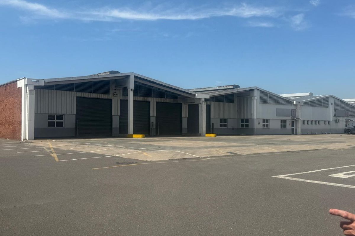 Industrial warehouse facility featuring multiple roller shutter doors, paved loading yard, and steel-framed structure with high-level ventilation.
