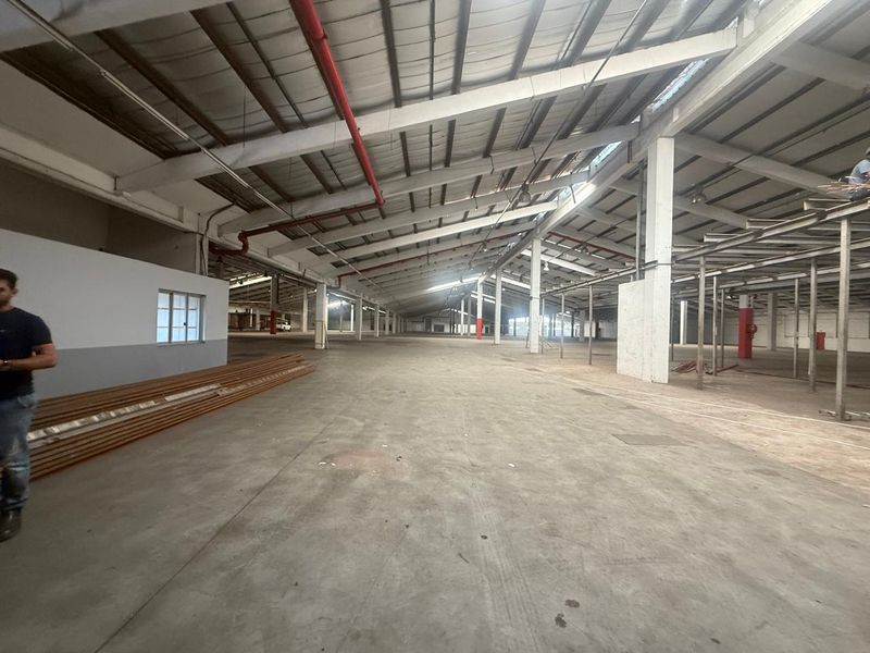 Expansive industrial warehouse space featuring high ceilings, exposed steel trusses, concrete flooring, and integrated fire suppression piping.