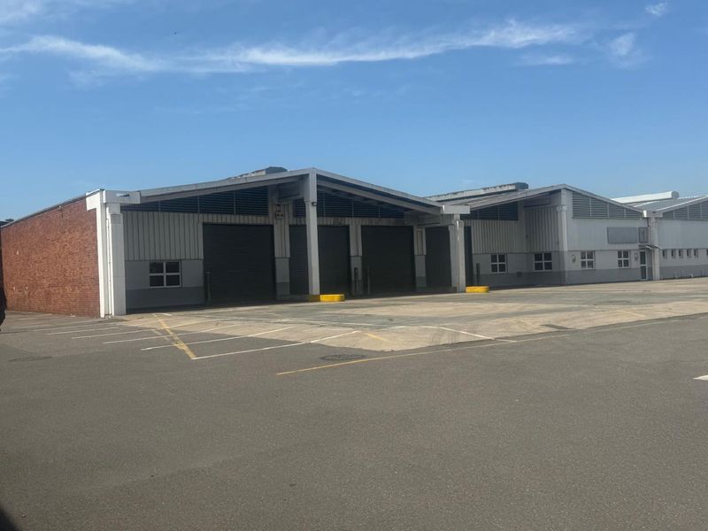 Industrial warehouse facility featuring multiple roller shutter doors, expansive paved yard area, and functional steel-framed structure suitable for logistics or manufacturing operations.
