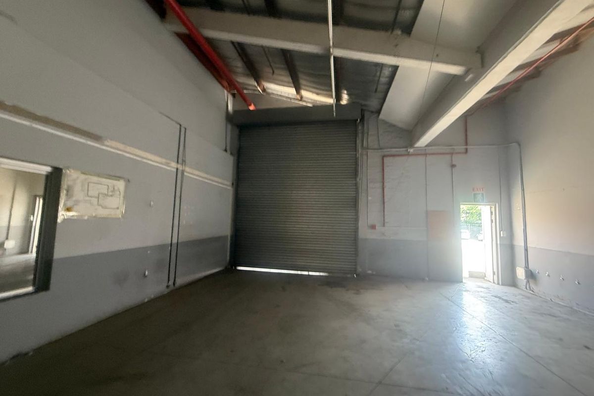 Spacious industrial warehouse unit featuring high ceilings, a large roller shutter door, and concrete flooring, suitable for various commercial or storage applications.