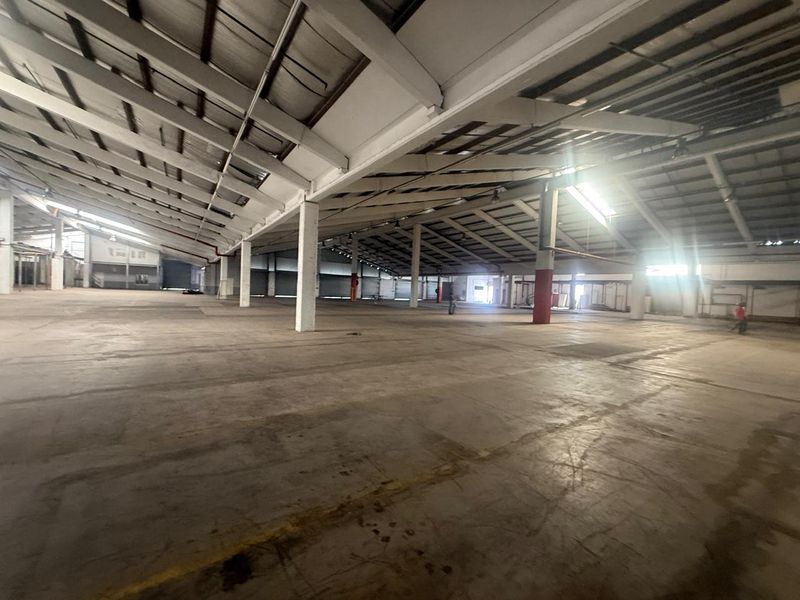 Expansive industrial warehouse space featuring high ceilings, exposed steel structural beams, and durable concrete flooring, suitable for various storage or manufacturing operations.