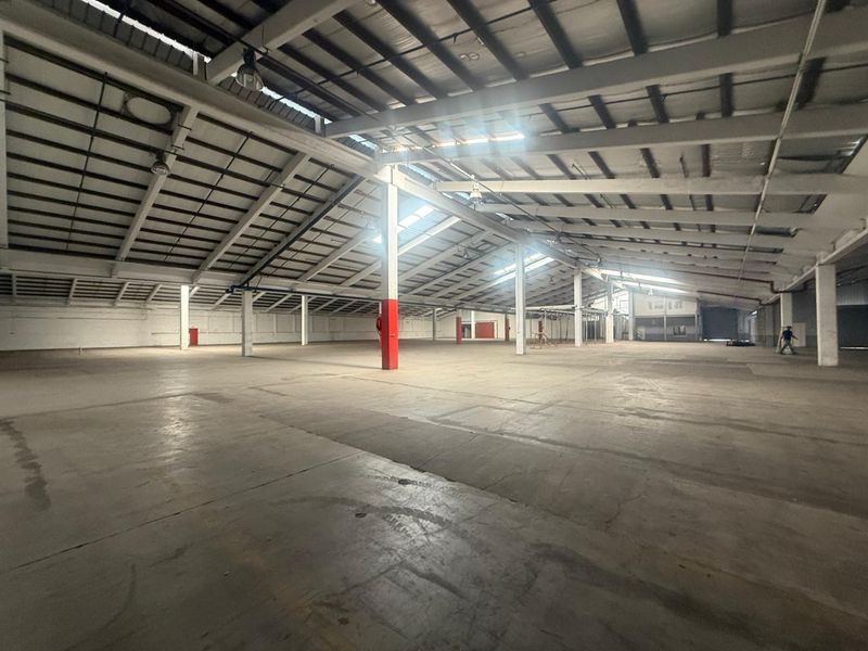 Expansive industrial warehouse space featuring high vaulted ceilings, exposed steel trusses, concrete flooring, and structural support columns.