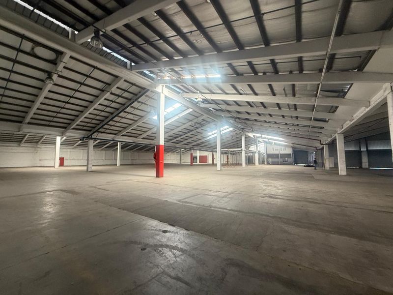 Expansive industrial warehouse space featuring high ceilings, exposed steel trusses, concrete flooring, and ample open floor area suitable for storage or manufacturing operations.