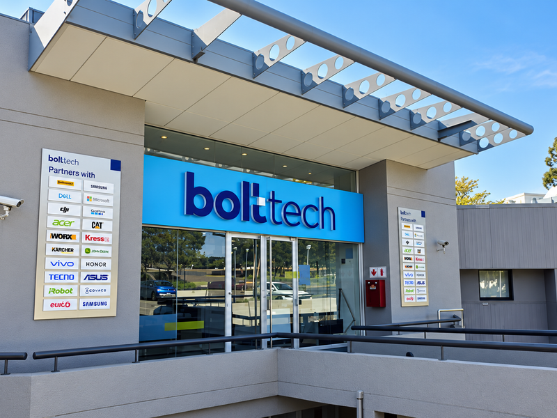 Modern industrial building entrance featuring a glass facade, metal awning, and prominent corporate signage.