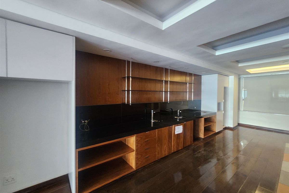 A modern office kitchenette featuring dark wood cabinetry, black stone countertops, double sinks, and integrated glass shelving with recessed ceiling lighting.