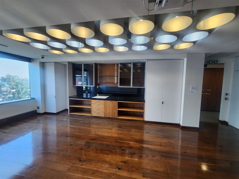 Modern office space featuring polished hardwood flooring, extensive built-in cabinetry with integrated sink, and a unique decorative ceiling lighting installation.