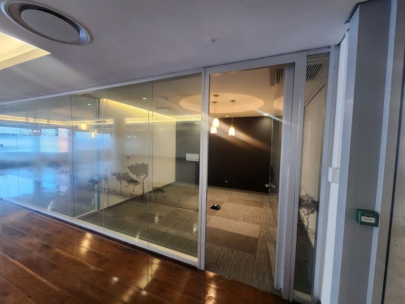 A modern office space featuring glass partition walls, recessed ceiling lighting, and carpeted flooring, providing a professional and bright work environment.