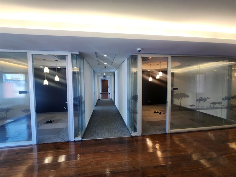 Modern office suite featuring glass-partitioned rooms, recessed and cove lighting, and a combination of hardwood and carpet flooring.