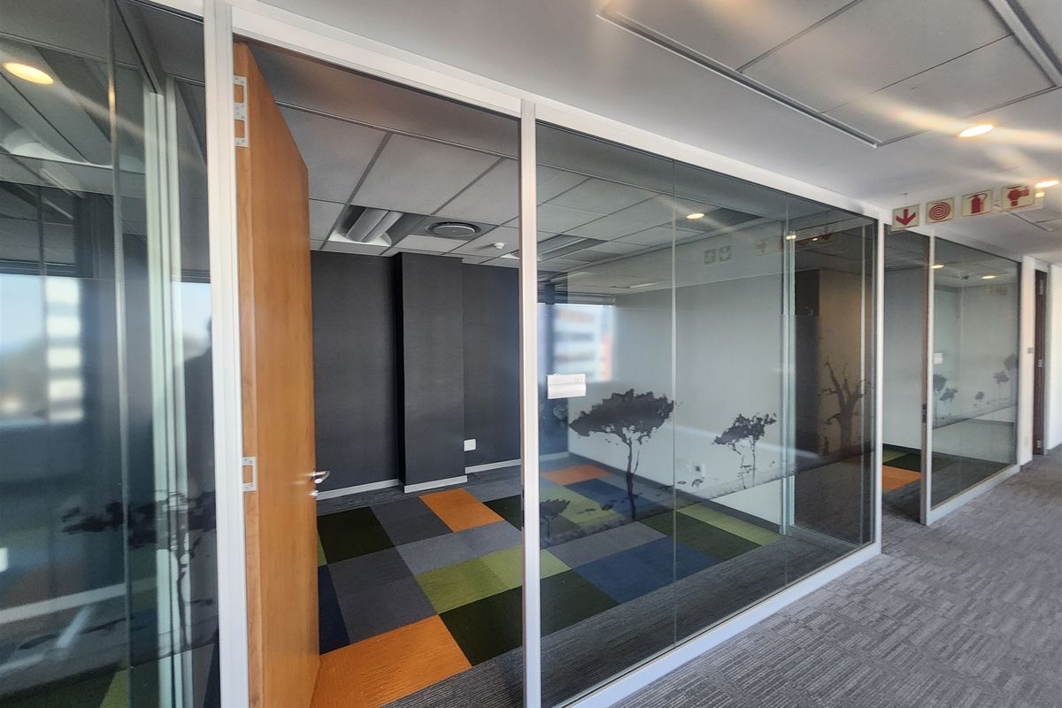 Modern office space featuring glass partition walls, suspended ceilings with recessed lighting, and colorful modular carpet tiles in a professional commercial setting.
