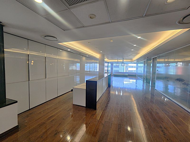 Spacious modern office interior featuring polished hardwood flooring, extensive built-in cabinetry, glass partitions, and recessed ceiling lighting with integrated air conditioning.