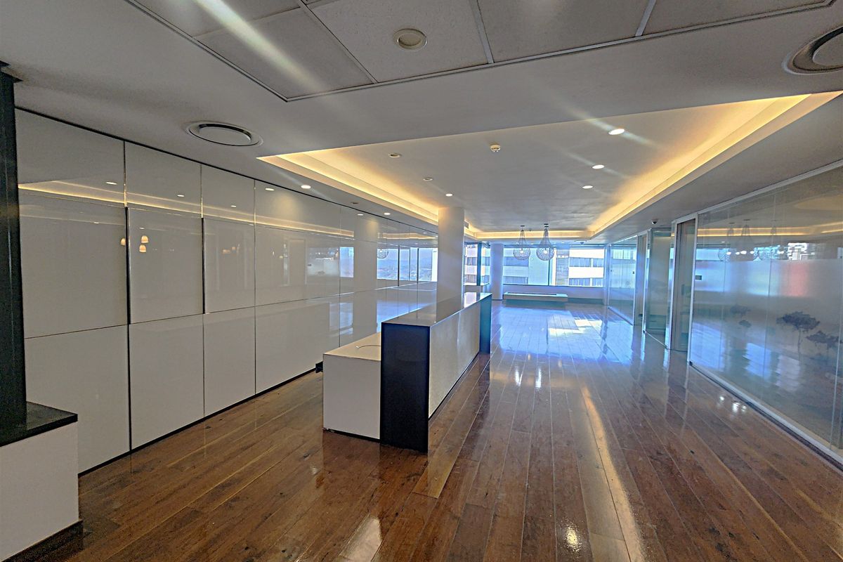 Spacious modern office interior featuring polished hardwood flooring, extensive built-in cabinetry, glass partitions, and recessed ceiling lighting with integrated air conditioning.
