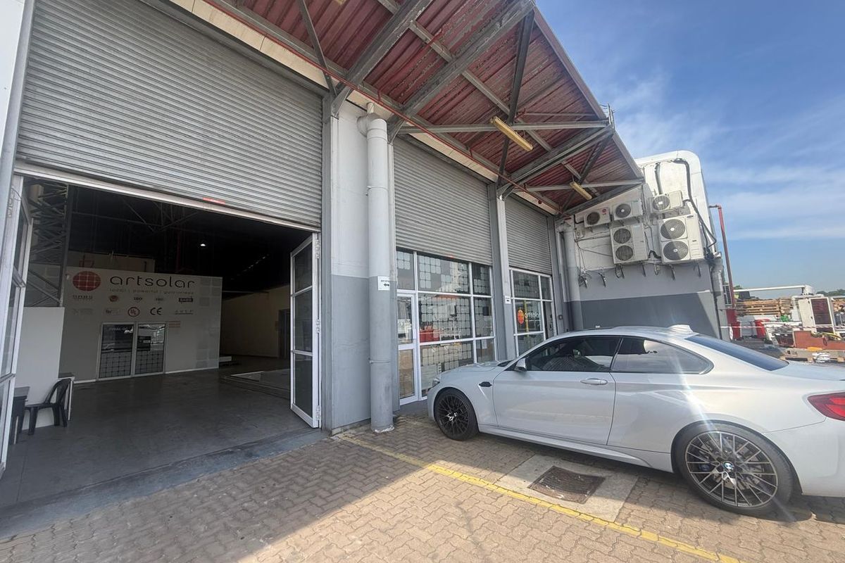 Industrial facility exterior featuring large roller shutter doors, paved driveway access, and multiple wall-mounted HVAC condenser units.