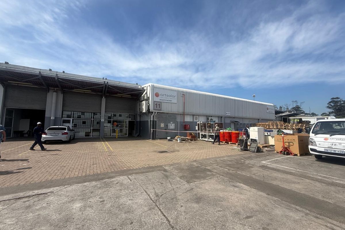 Exterior view of an industrial facility featuring a large warehouse structure with roller shutter doors and paved yard area.