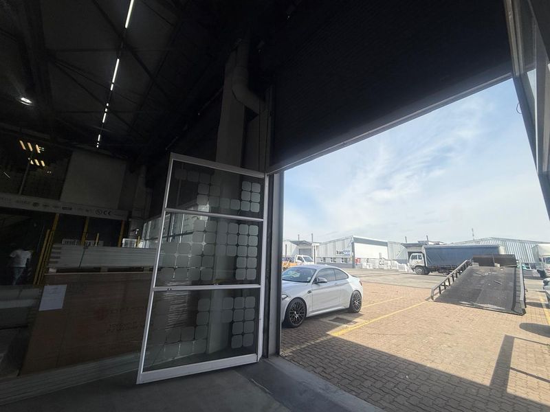 Industrial warehouse interior featuring a large roller shutter door opening to an external paved loading area and parking space.
