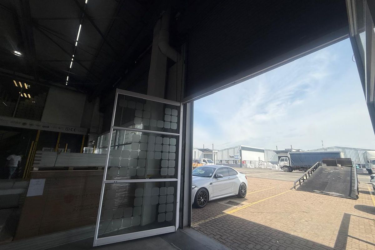Industrial warehouse interior featuring a large roller shutter door opening to an external paved loading area and parking space.