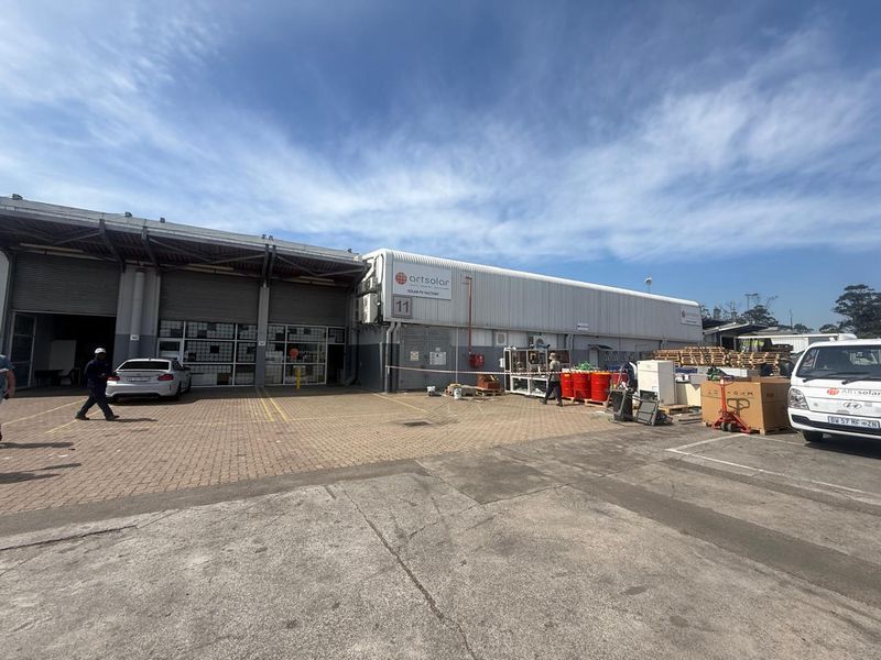 Exterior view of an industrial facility featuring a large warehouse structure with roller shutter doors and paved yard area.