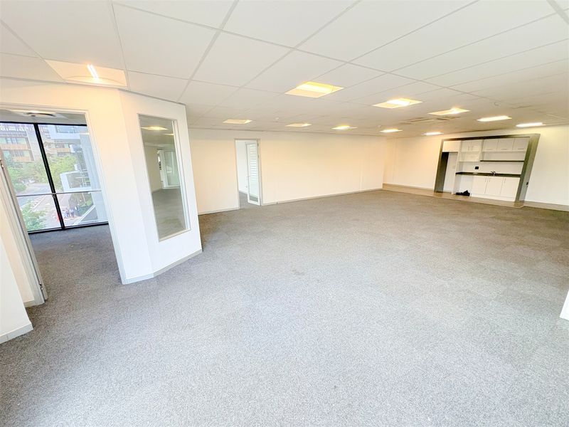 Spacious open-plan office area featuring a suspended ceiling, recessed lighting, carpeted flooring, and a convenient built-in kitchenette.