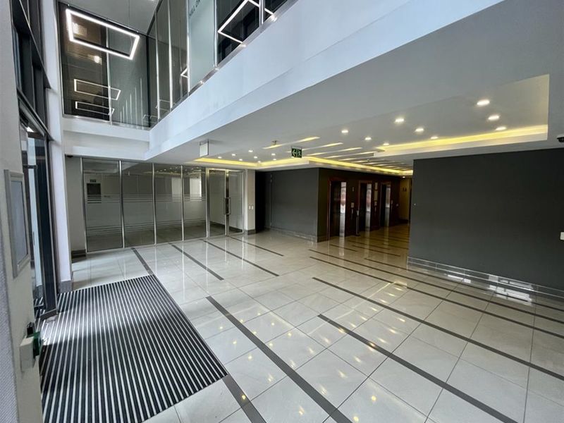 Modern, spacious office building lobby featuring high ceilings, polished tiled flooring, glass partitions, and a professional elevator bank area.