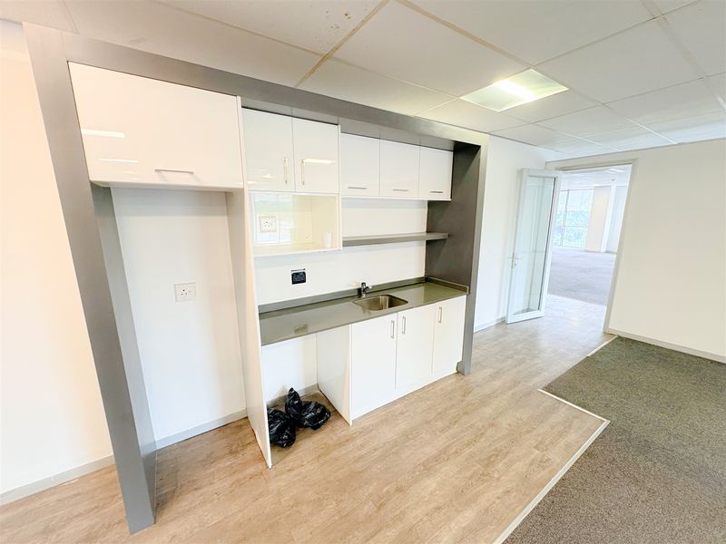 A compact office kitchenette featuring white cabinetry, a stainless steel sink, and laminate countertops, set within a professional workspace with drop ceilings.