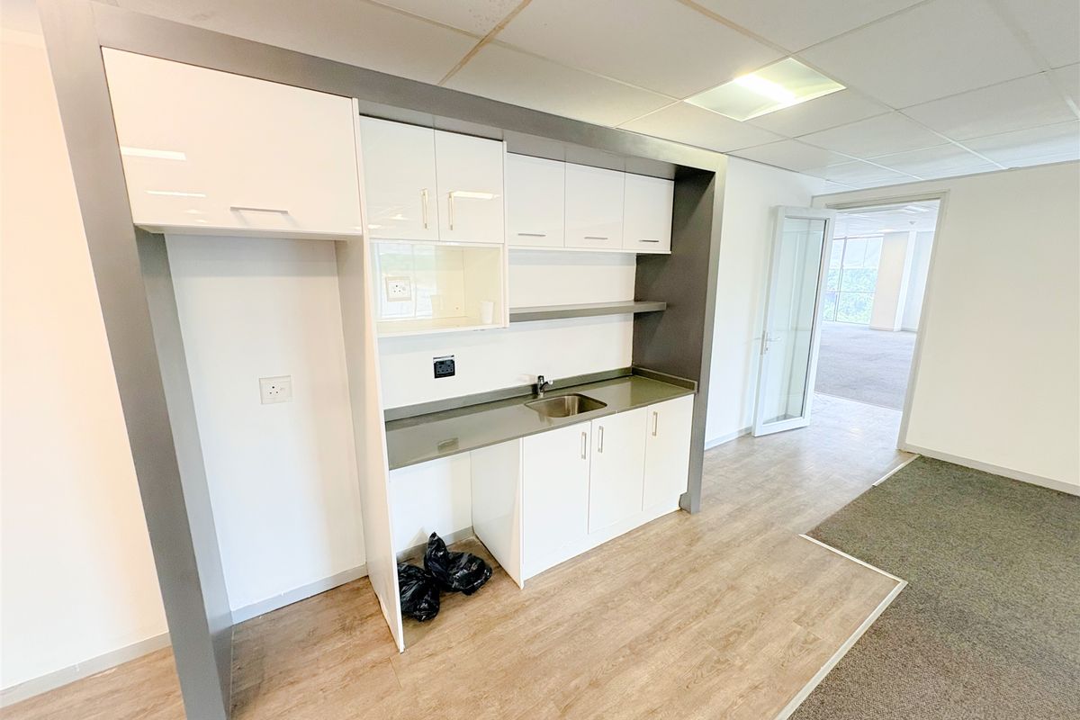 A compact office kitchenette featuring white cabinetry, a stainless steel sink, and laminate countertops, set within a professional workspace with drop ceilings.