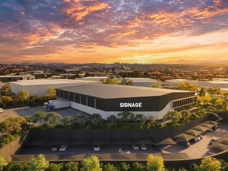 Aerial view of a modern industrial warehouse facility featuring a loading bay, extensive covered parking, and well-maintained landscaped grounds at sunset.