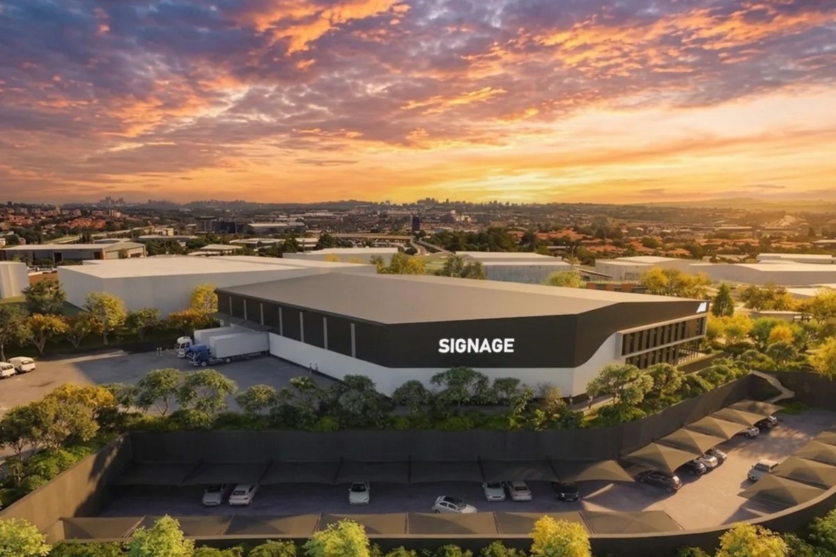 Aerial view of a modern industrial warehouse facility featuring a loading bay, extensive covered parking, and well-maintained landscaped grounds at sunset.