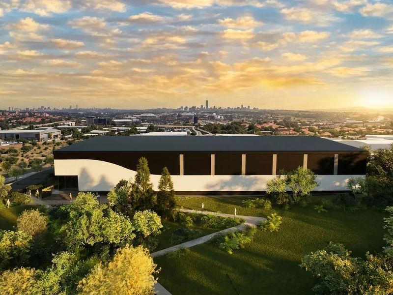 Aerial view of a modern industrial warehouse facility set within landscaped grounds, featuring a clean architectural design and expansive surrounding area.