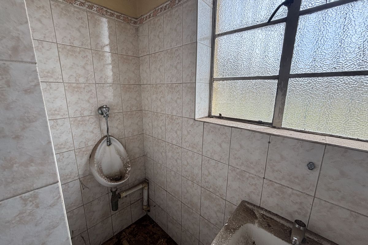A dated bathroom facility featuring a wall-mounted urinal, basin, and tiled walls, currently requiring significant maintenance and refurbishment.