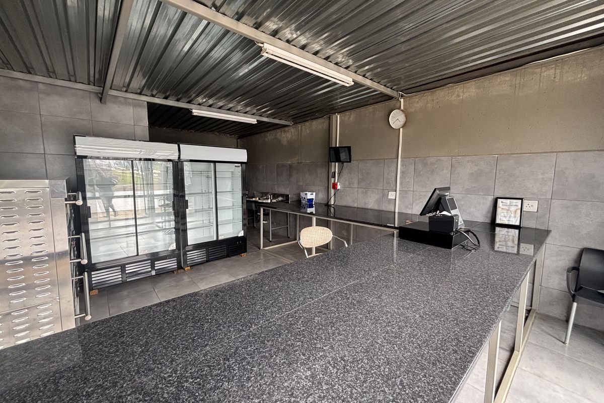A functional retail kitchen space featuring granite countertops, tiled wall finishes, and a corrugated metal ceiling, suitable for food preparation or service.