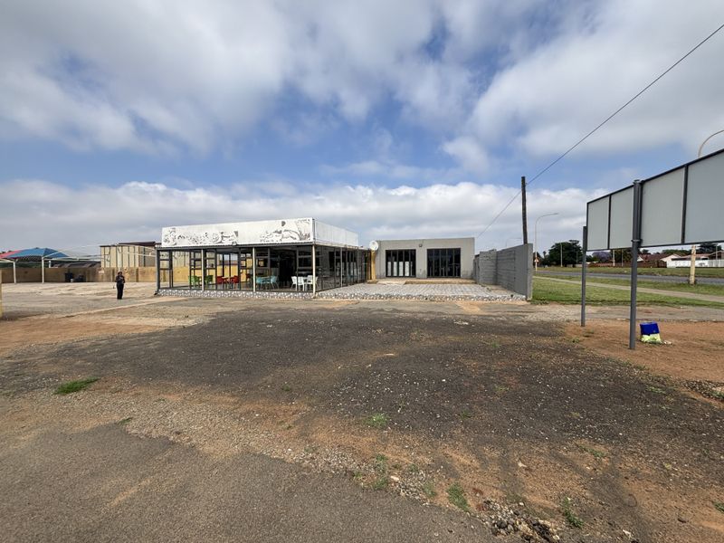 Front view of a commercial retail property featuring a large glass facade, signage area, and an expansive unpaved forecourt.