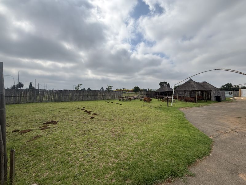 Spacious outdoor area featuring a large lawn, paved driveway, and multiple thatched gazebos enclosed by timber fencing.