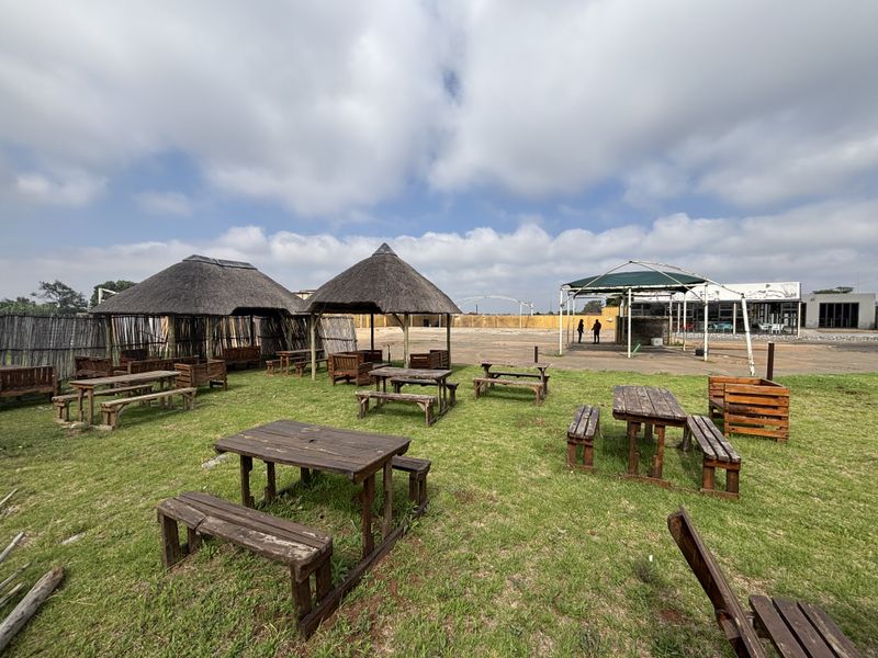 Outdoor entertainment area featuring thatched gazebos, a metal-framed canopy, and open lawn space, suitable for retail or hospitality use.
