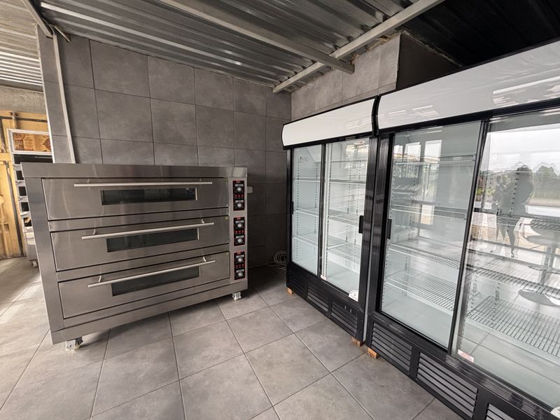 A commercial kitchen space featuring a triple-deck oven and dual glass-door display refrigerators, finished with tiled walls and flooring.