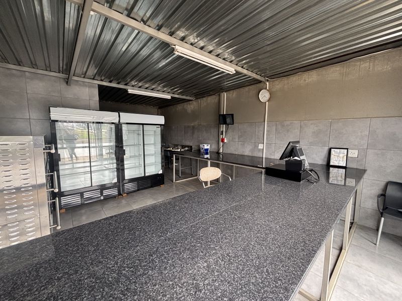 A functional retail kitchen space featuring granite countertops, tiled wall finishes, and a corrugated metal ceiling, suitable for food preparation or service.