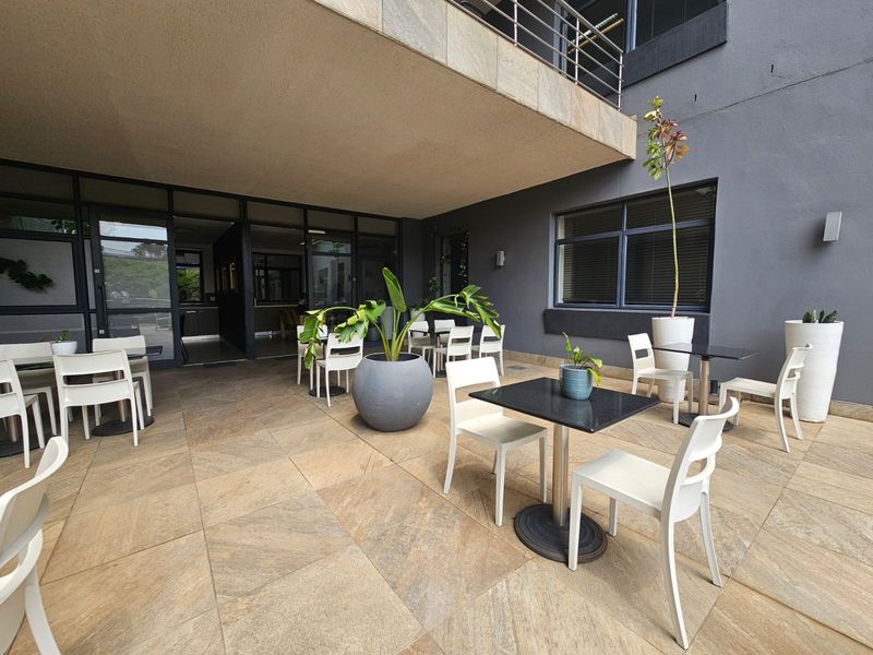 A covered outdoor patio area featuring large format floor tiles, stone-clad architectural detailing, and direct access to the interior office or business space.