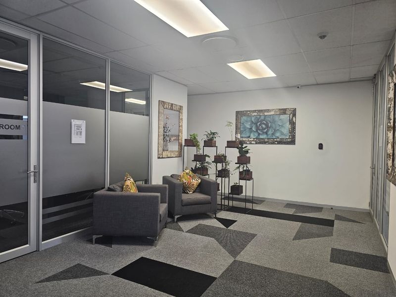 A professional office reception or waiting area featuring glass partitions, modern patterned carpet tiles, and recessed ceiling lighting.