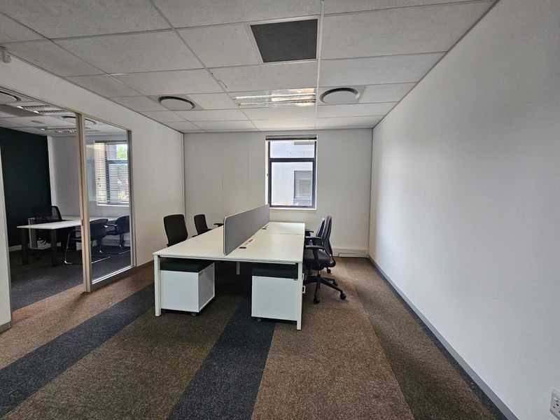 A professional office space featuring carpeted flooring, a suspended ceiling with recessed lighting, and a glass partition separating the work area.