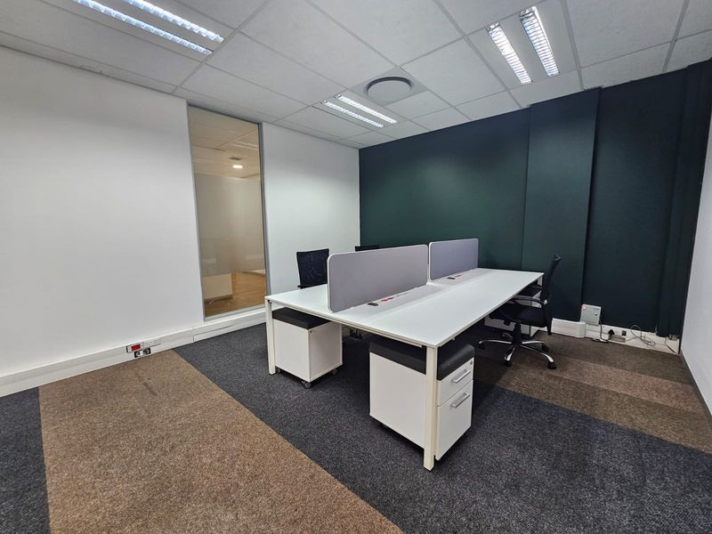 A modern, well-lit office space featuring carpeted flooring, a glass partition, and a neutral color palette with a dark accent wall.