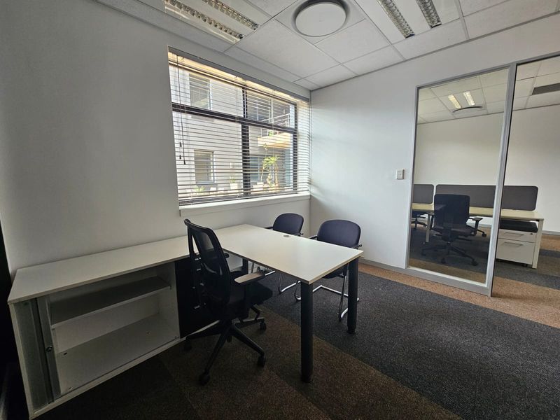 A functional office space featuring carpeted flooring, a suspended ceiling with integrated lighting, and a glass partition wall providing a professional work environment.