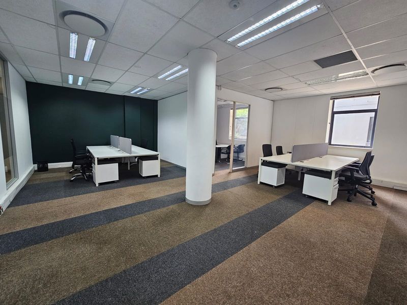 Open-plan office space featuring a suspended ceiling, recessed lighting, structural column, and carpeted flooring with glass partition access to an adjacent room.