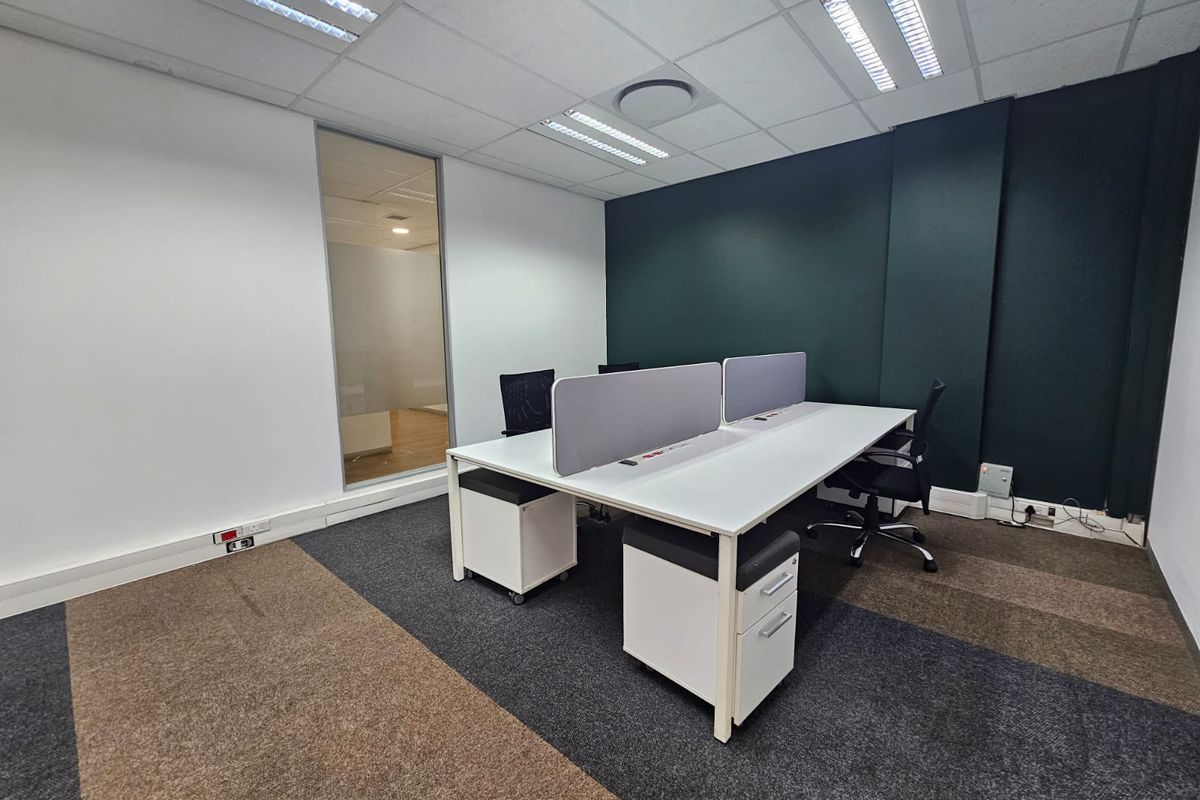 A modern, well-lit office space featuring carpeted flooring, a glass partition, and a neutral color palette with a dark accent wall.