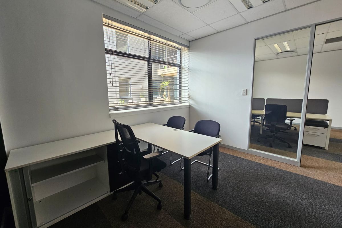 A functional office space featuring carpeted flooring, a suspended ceiling with integrated lighting, and a glass partition wall providing a professional work environment.